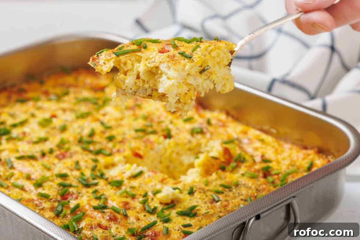 19 Fall Cookout Recipes for Sunday Dinner and Game Day 3 A Corn Pudding Casserole topped with chopped chives in a metal baking dish, with a portion being lifted out on a serving spatula.