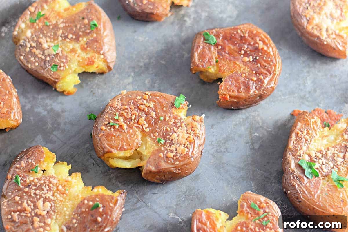 19 Fall Cookout Recipes for Sunday Dinner and Game Day 21 Crispy Garlic Parmesan Smashed Potatoes topped with herbs and grated cheese on a metal baking sheet.