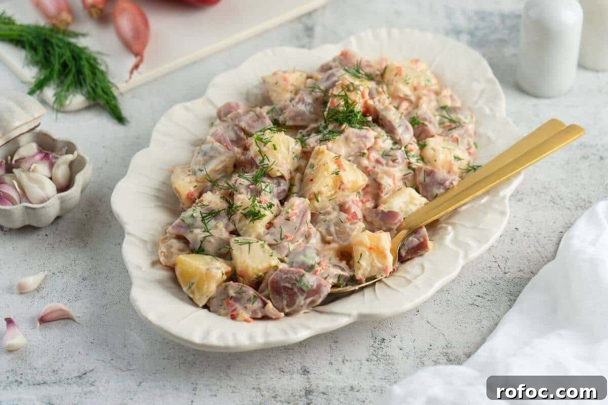 19 Fall Cookout Recipes for Sunday Dinner and Game Day 7 A serving dish filled with Classic Red Potato Salad with Pickles is garnished with fresh dill, with a gold-colored serving spoon resting in the dish.