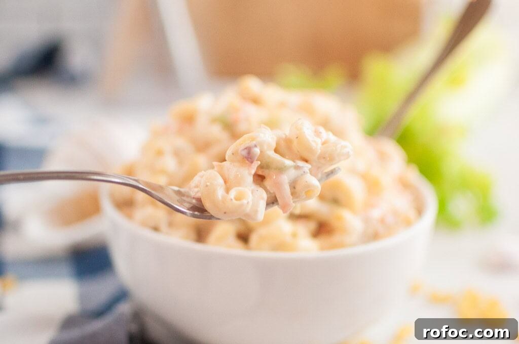 19 Fall Cookout Recipes for Sunday Dinner and Game Day 9 A close-up shot of a fork lifting a portion of macaroni salad, with a bowl of the salad in the blurred background.