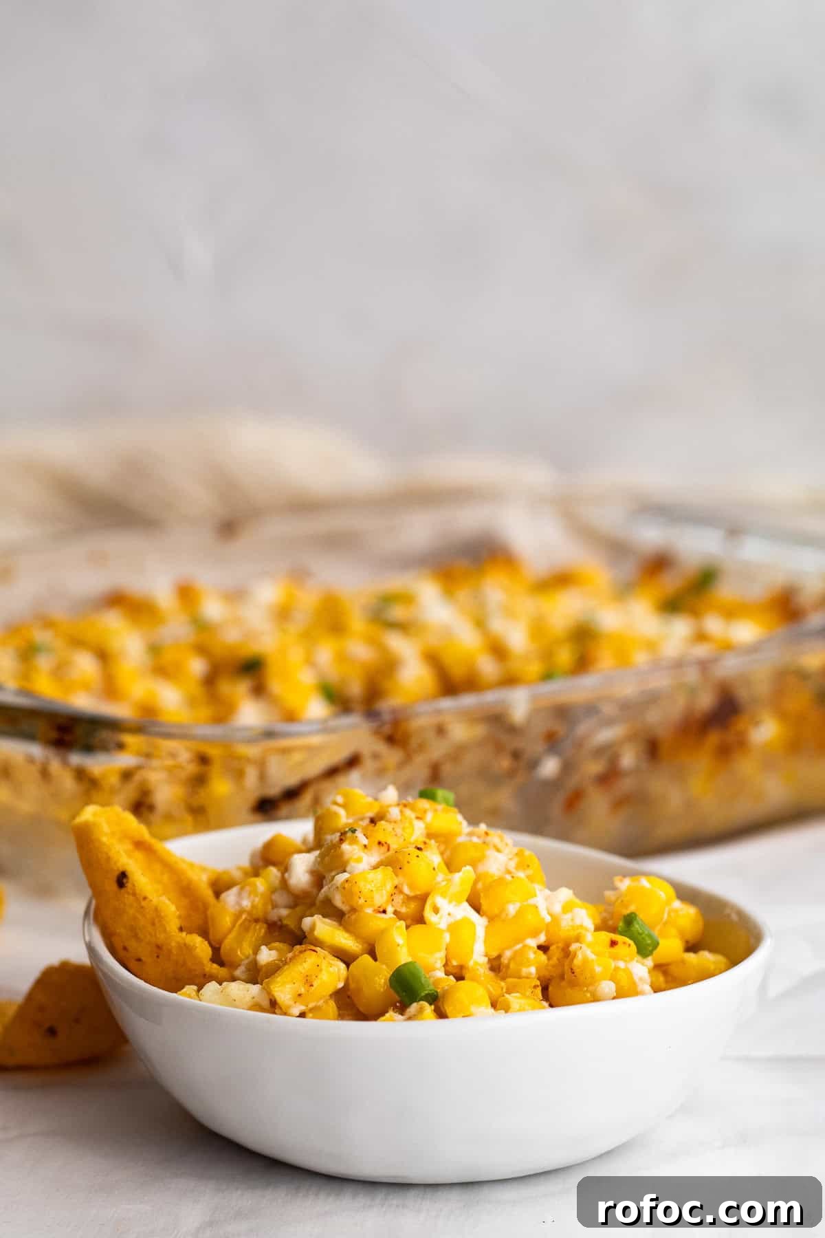 6-Ingredient Mexican Street Corn Casserole Recipe 2 white bowl of mexican street corn with a corn chip in it and the pan behine