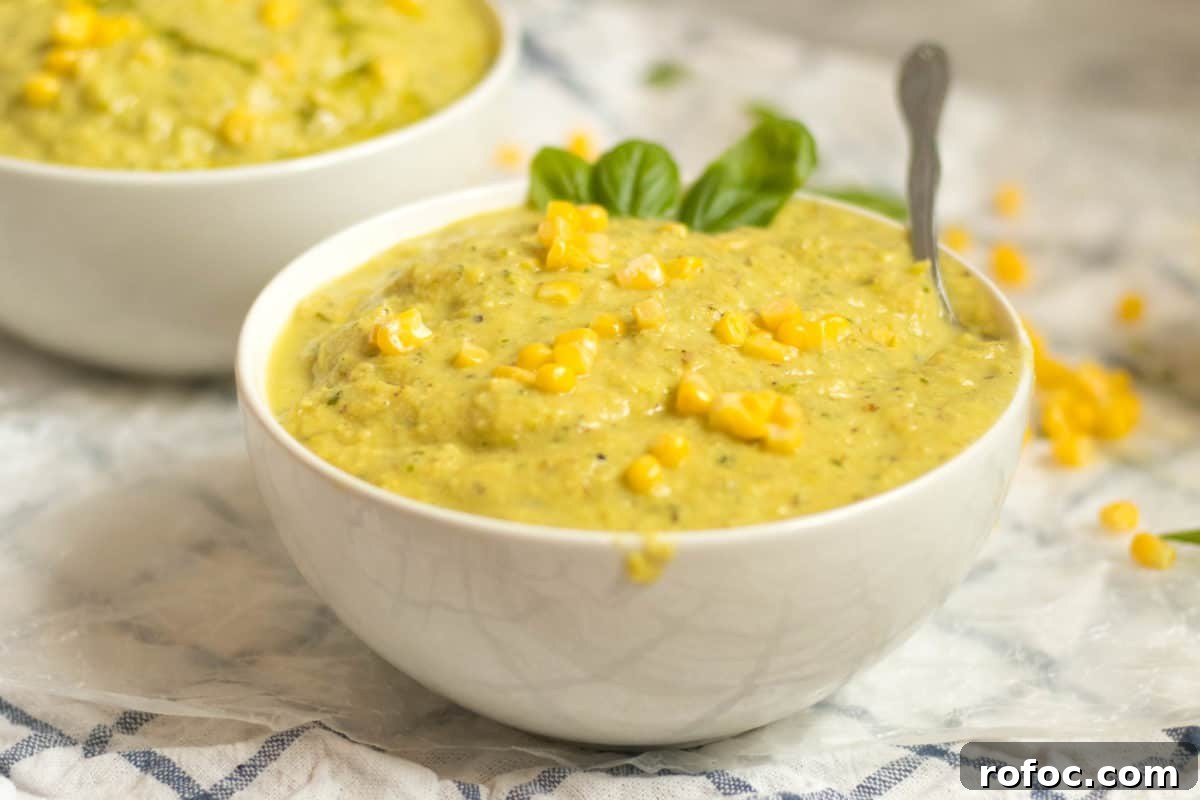 white bowl filled with corn and basil soup with corn kernels and basil leaves for garnish