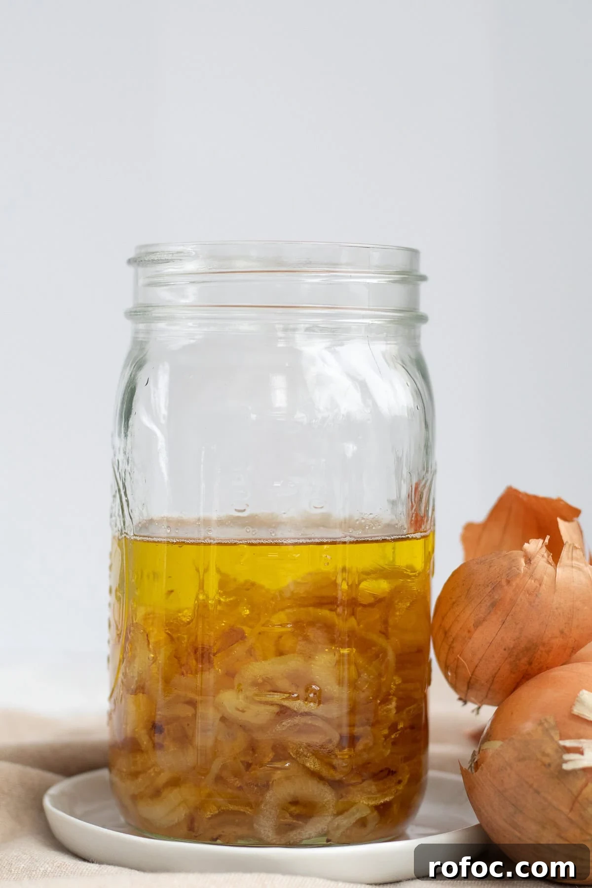 mason jar of onion oil with whole yellow onions next to it