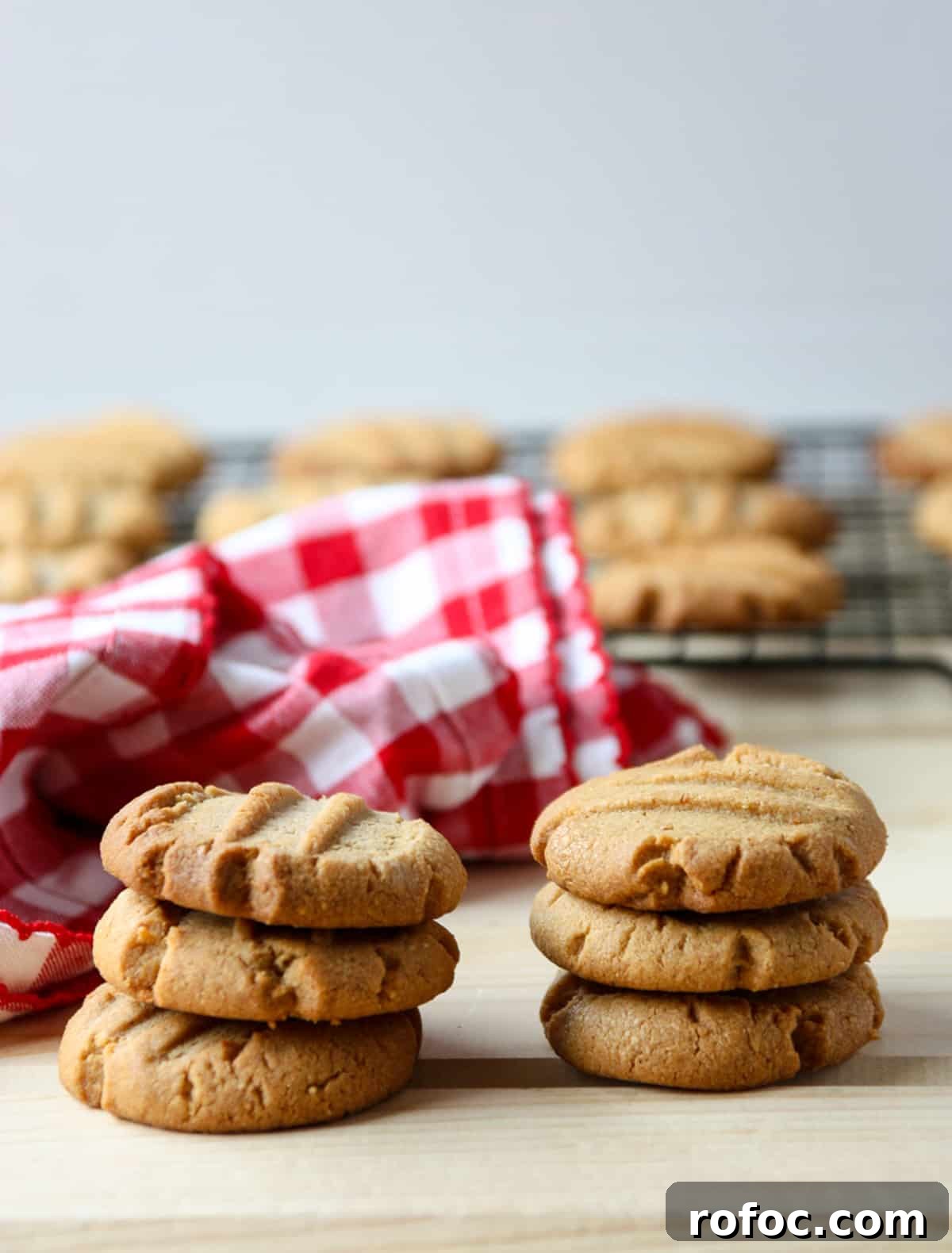 Two stacks of three peanut butter cookies on a wooden table beside a red and white napkin.