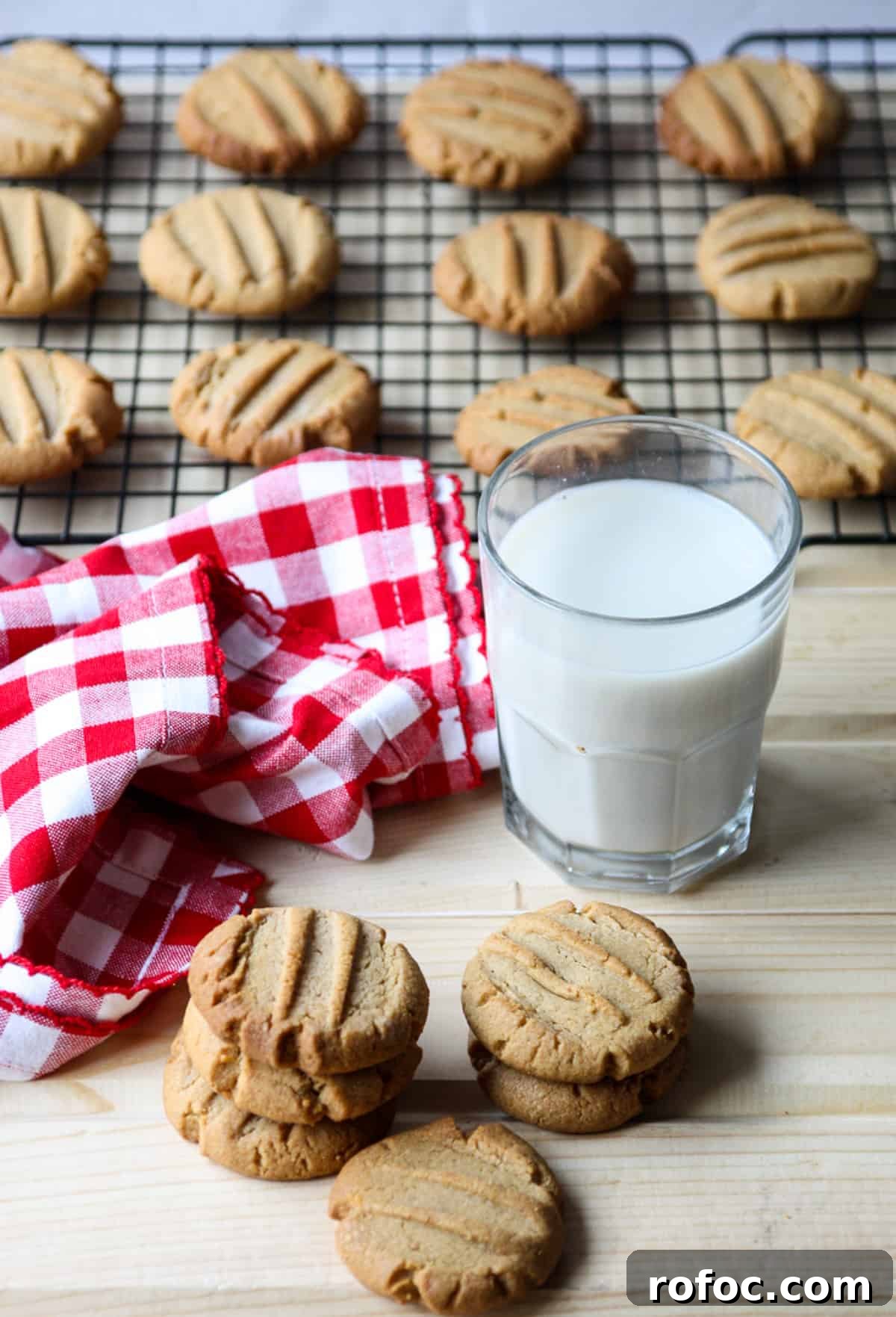 Gluten free peanut butter cookies and a glass of milk, in front of a wire rack with cookies cooling.