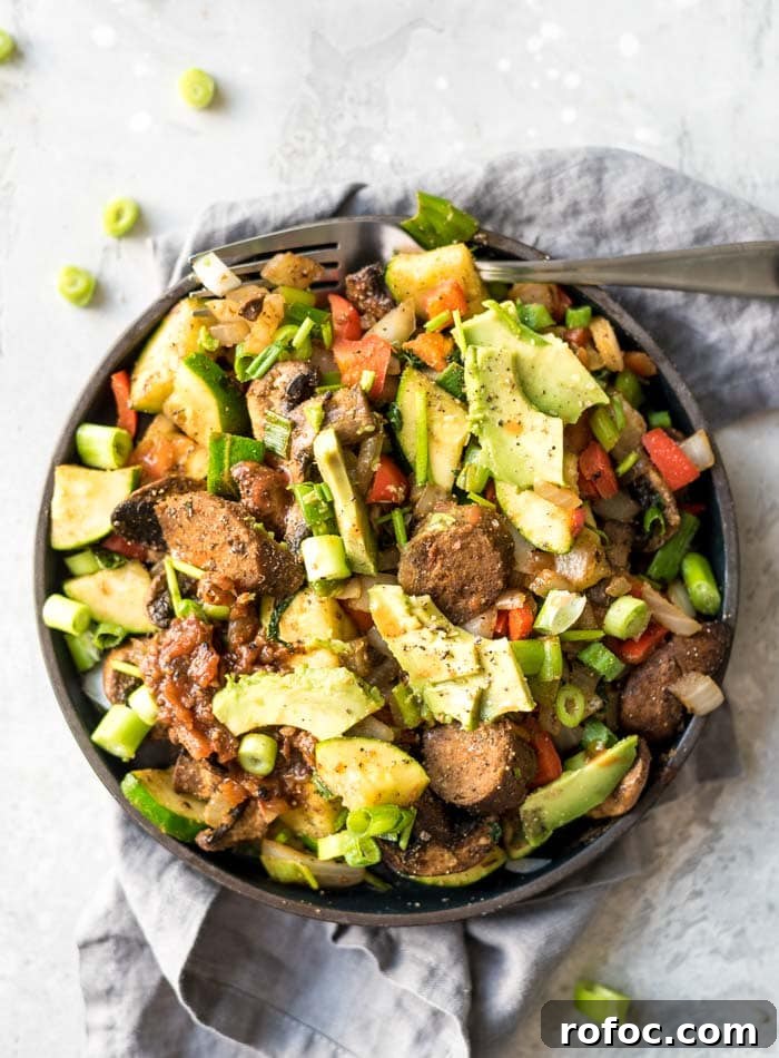 Plate of a breakfast skillet with vegetables, vegan sausage, avocado and salsa.