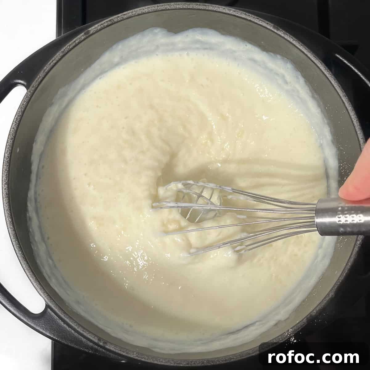 Whisking melkkos in a black saucepan.