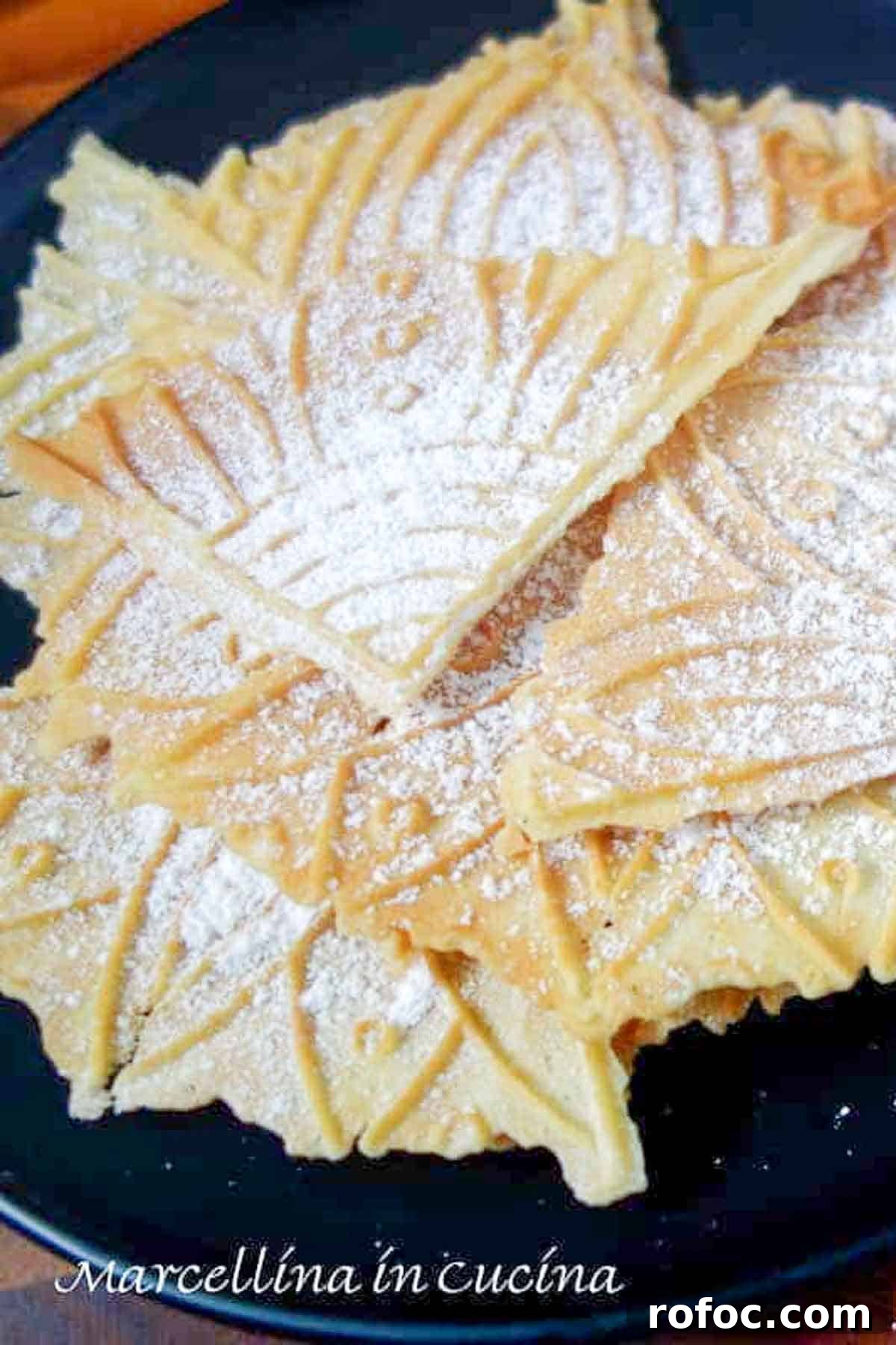 Lemon pizzelle dusted with powdered sugar on a black plate.