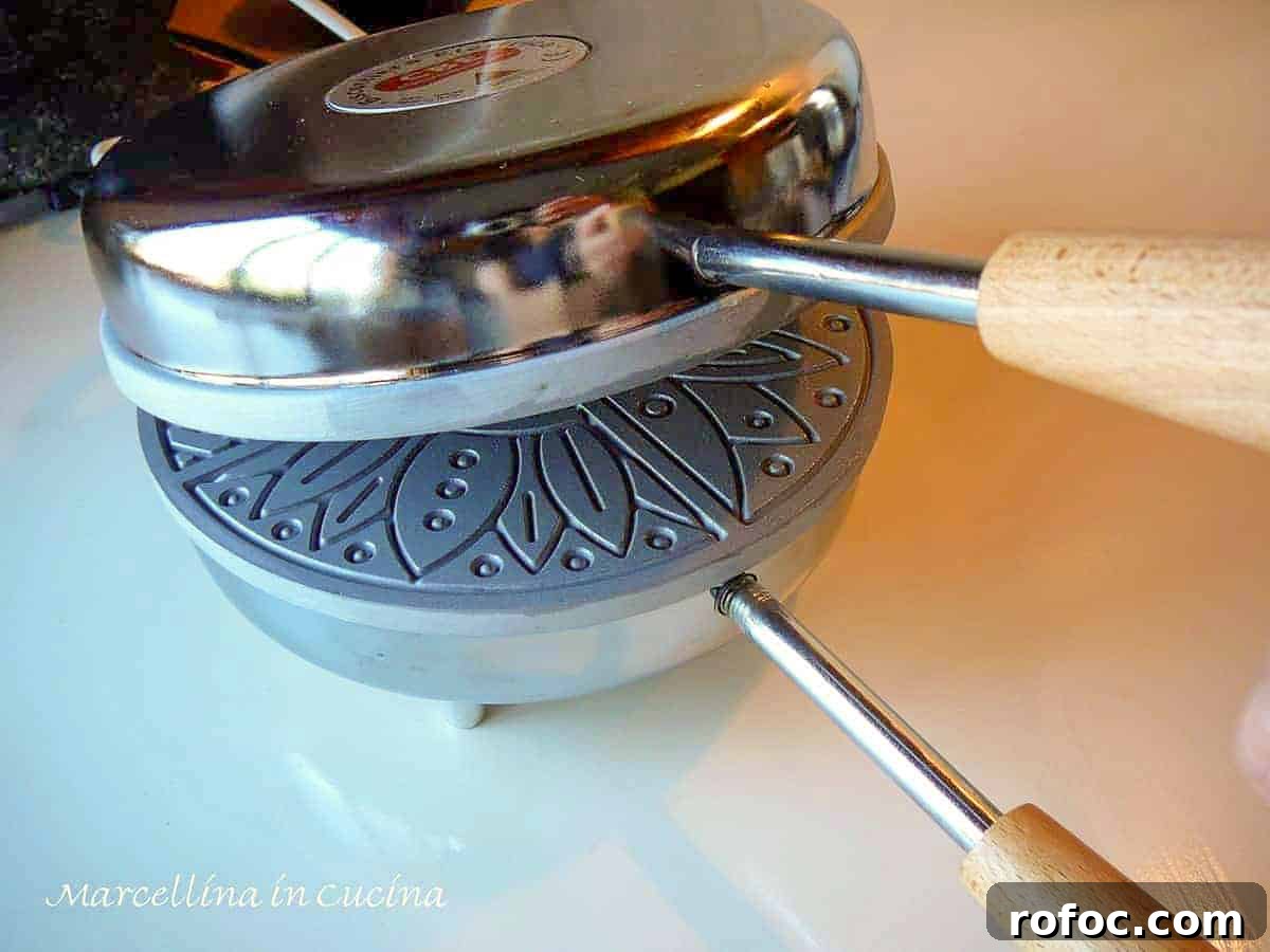 a stainless steel pizzelle iron partially opened showing the griddle inside.