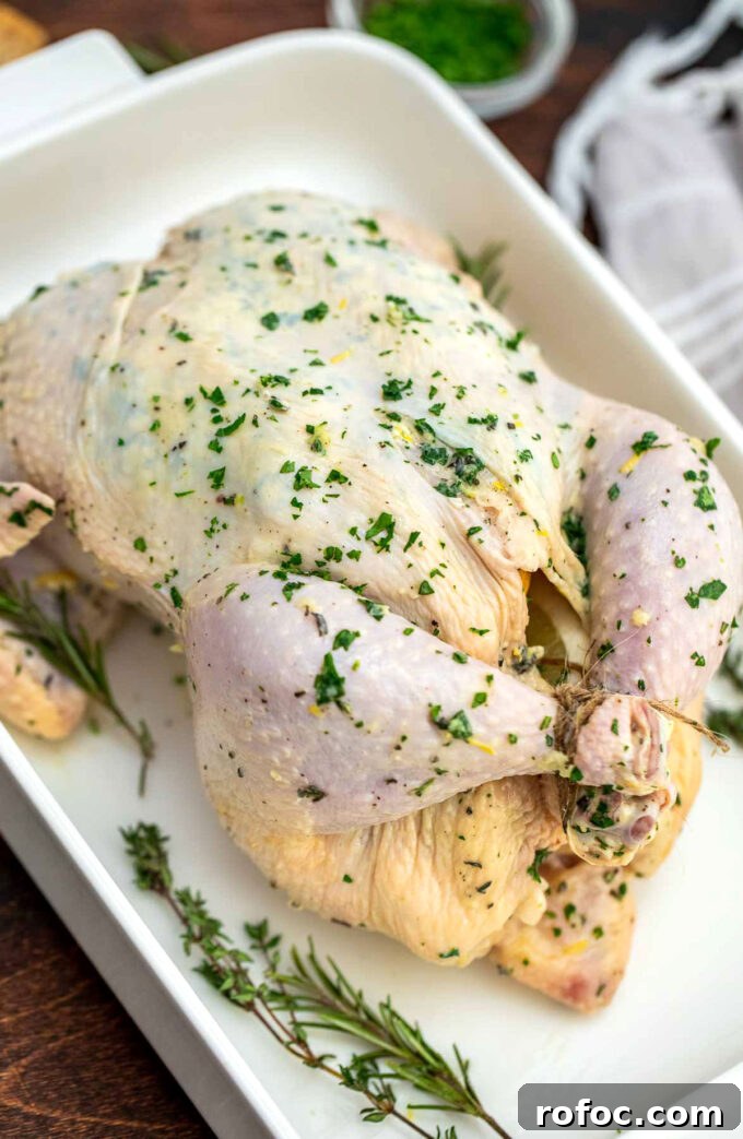 Whole chicken covered in garlic butter and herbs in a baking dish.