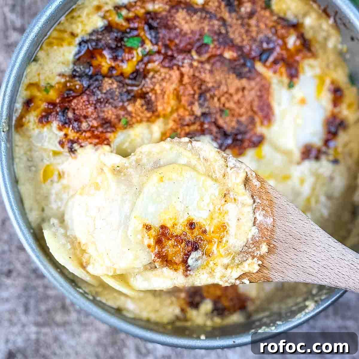 A wooden spoon lifting a serving of golden, tender scalloped potatoes, showcasing the creamy sauce and melted cheese topping.