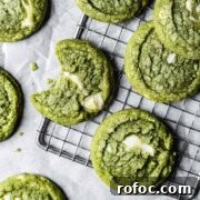 A close up of green drop cookies with white chocolate chunks on a metal cooling rack.