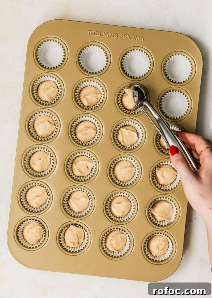 Mini Vanilla Cupcakes: Tender Bite-Sized Recipe 8 A hand using a scoop to divide vanilla cupcake batter into a mini cupcakes pan.