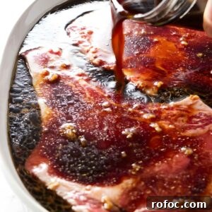 Hand pours dark marinade over raw beef steaks.