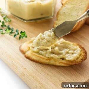 Knife spreading roasted garlic on toast.