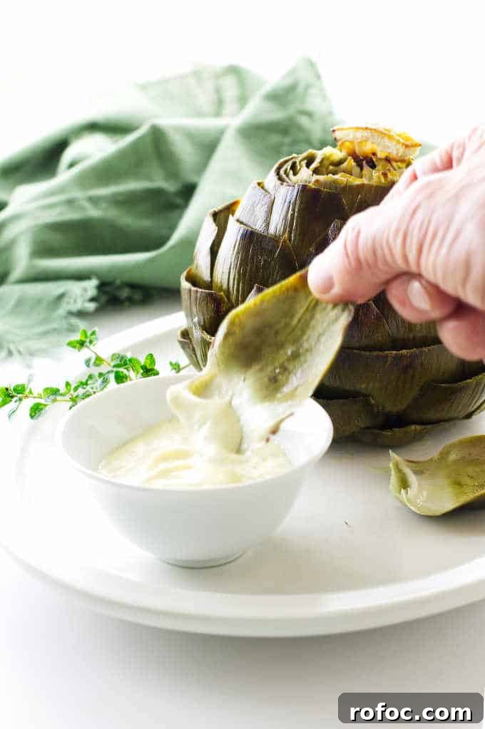 Artichoke leaf being dipped into garlic-lemon aioli sauce