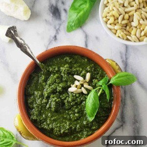 A bowl filled with basil pesto next to pine nuts.