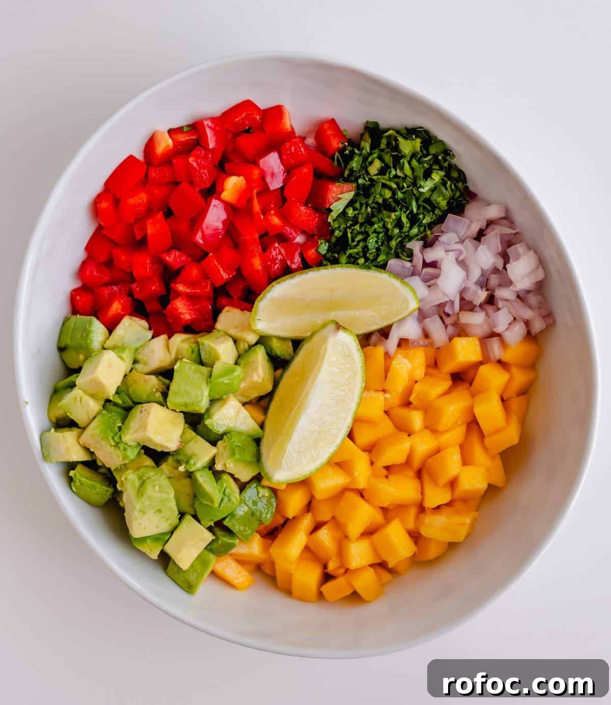 Make mango avocado salsa ingredients in a bowl - diced avocado, bell pepper, mango, onion, cilantro, and lime wedges