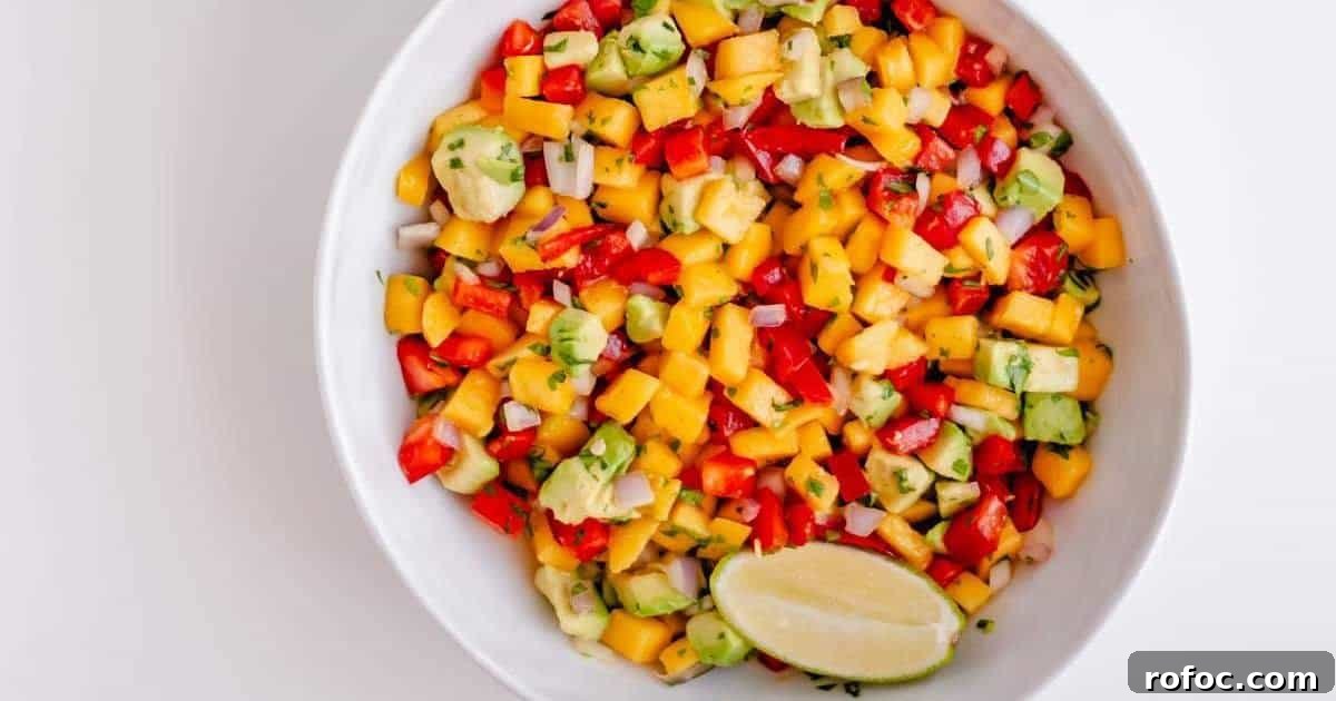 A bowl of mango and avocado salsa with a lime wedge.