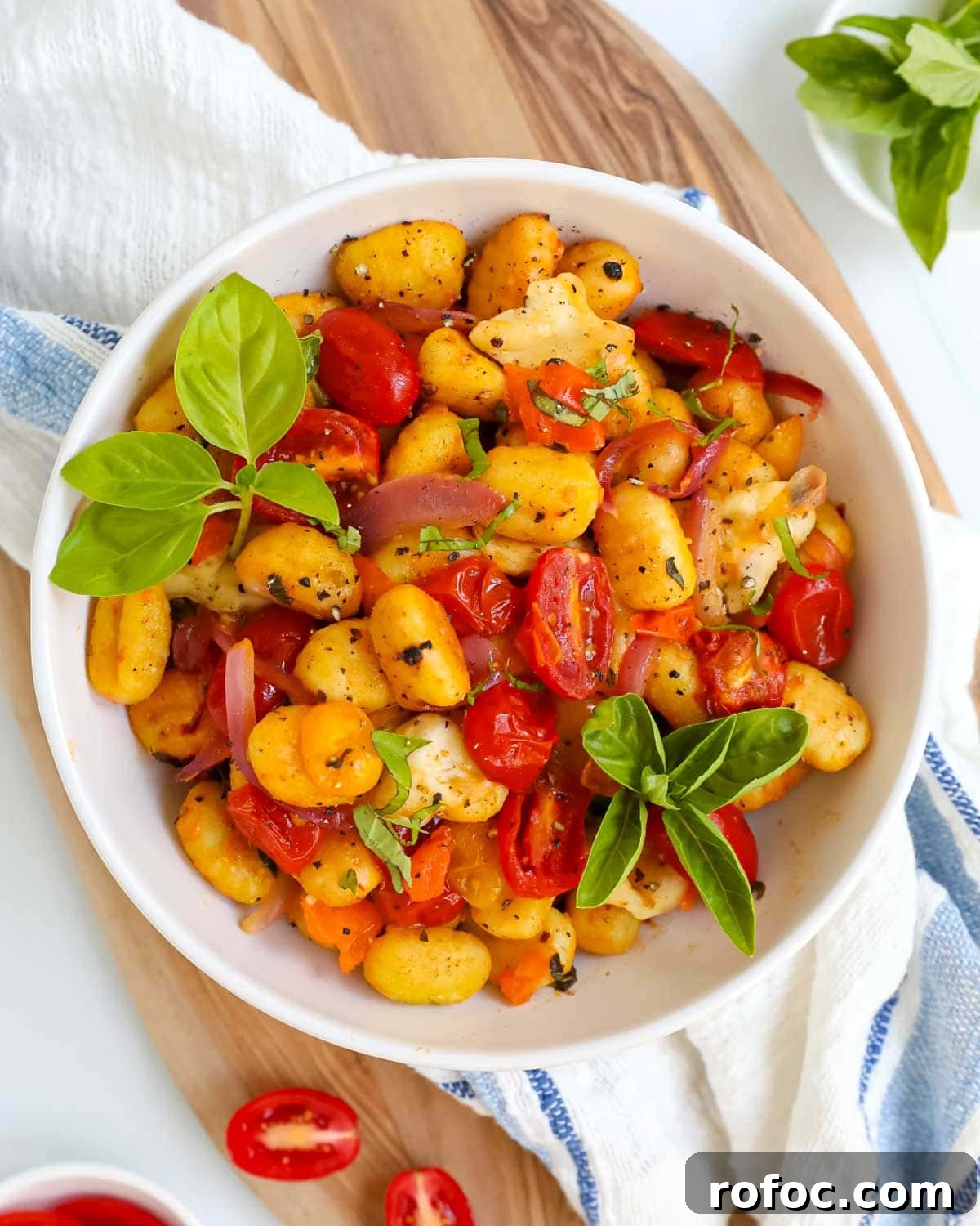 Crispy Sheet Pan Gnocchi with Roasted Vegetables 2 Gnocchi with tomatoes, onion, and basil in a white bowl.