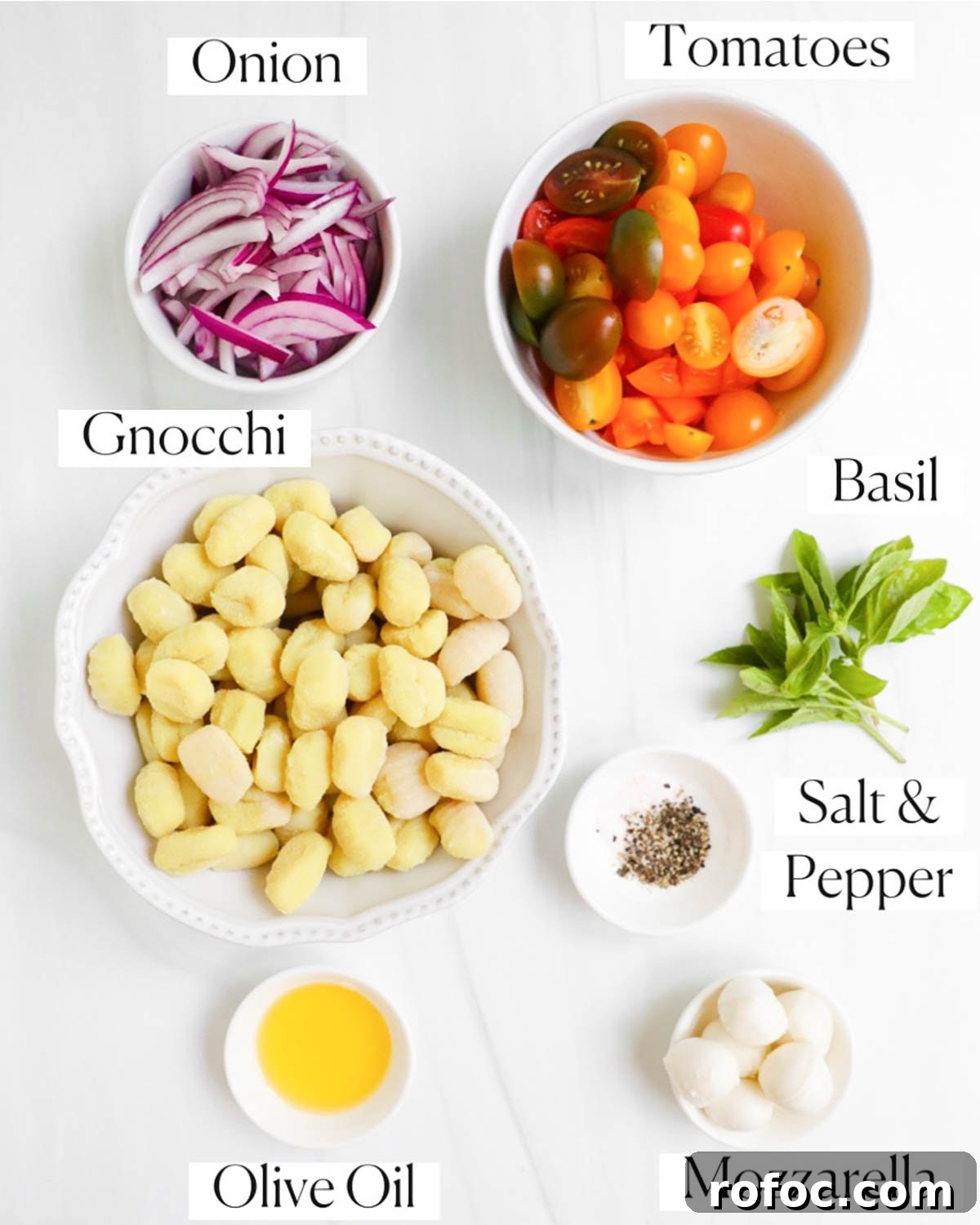 Crispy Sheet Pan Gnocchi with Roasted Vegetables 3 Labeled ingredients in small white bowls including: onion, tomatoes, gnocchi, basil, salt and pepper, olive oil, and mozzarella.